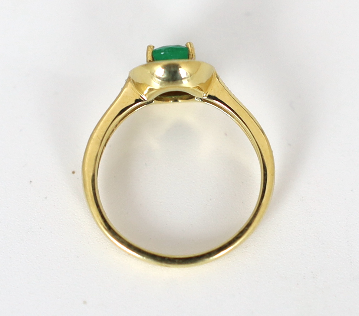 A modern 18ct gold, emerald and diamond set oval cluster ring, with diamond chip set shoulders